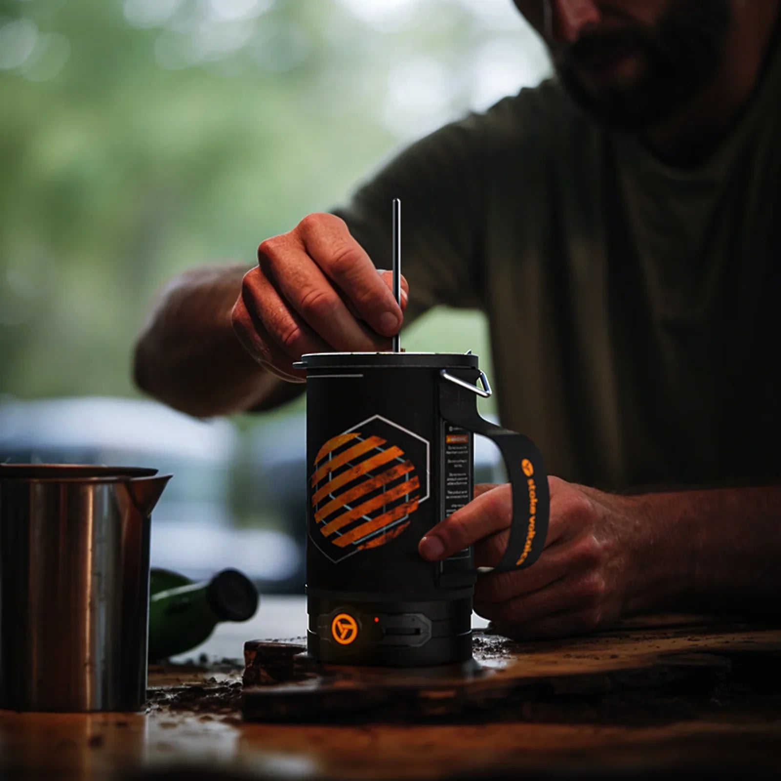 Man using Stoke Voltaics all-purpose kettle pot and french press outdoors on wooden table