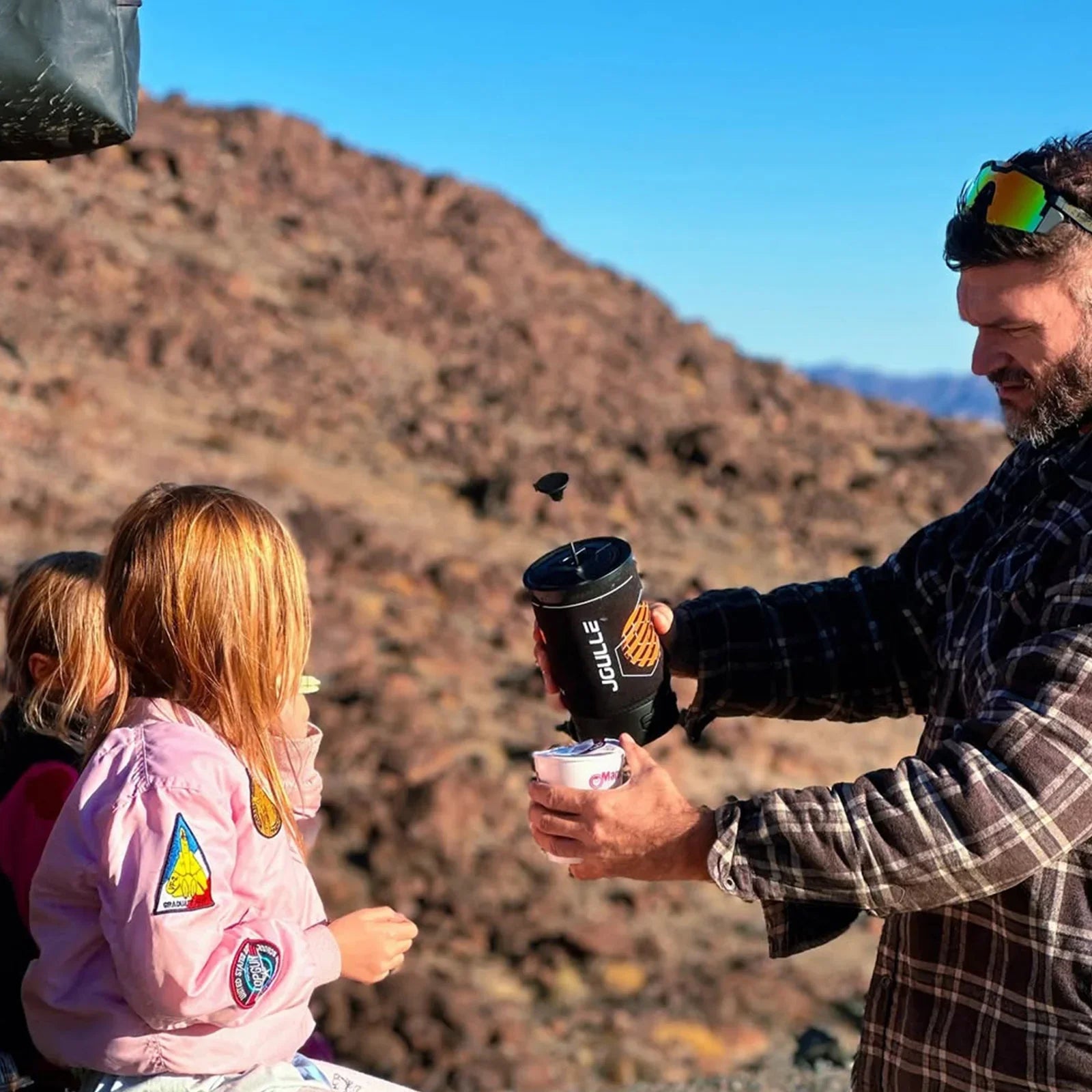 Man pours outdoor French press coffee into cup with kids in rocky wilderness, Stoke Voltaics
