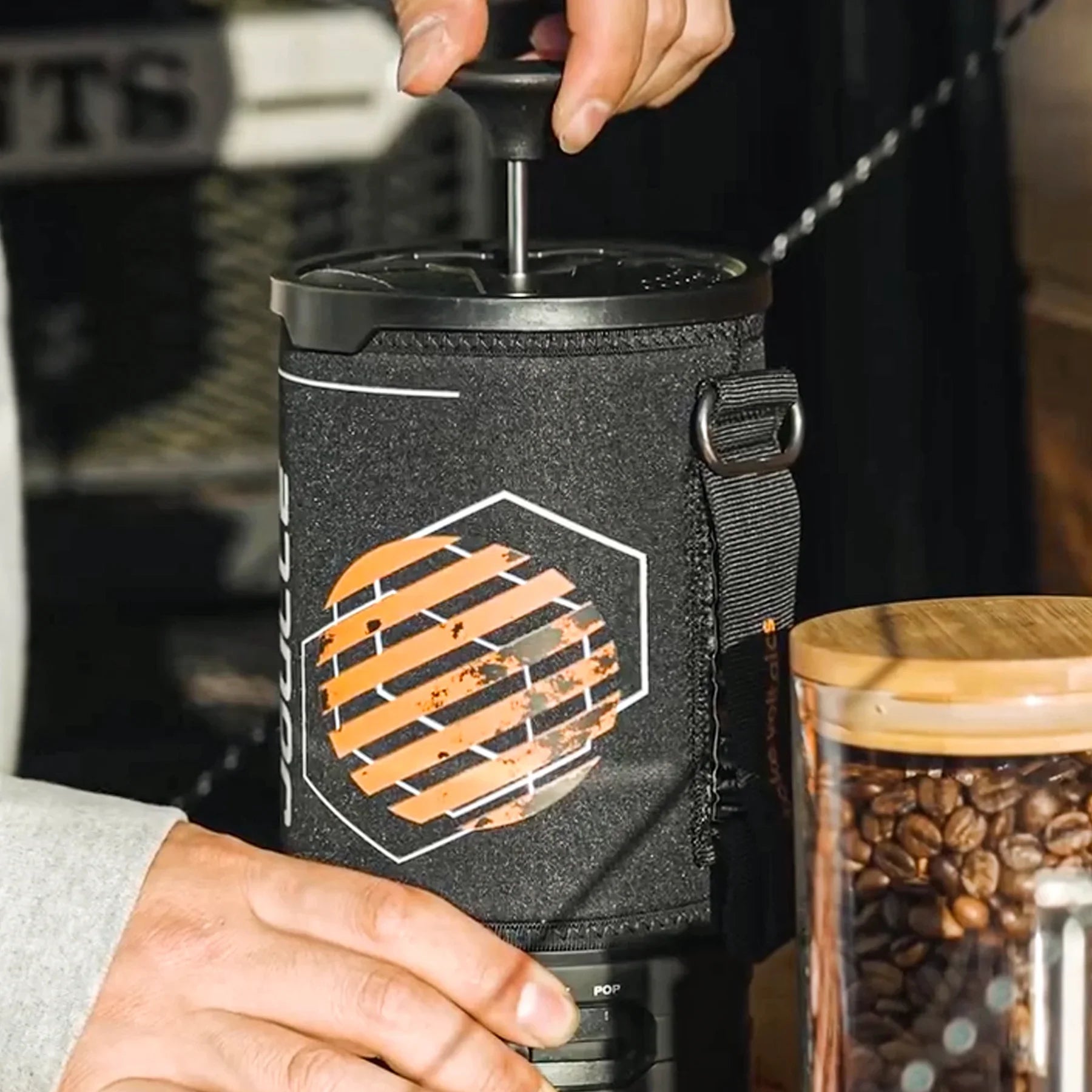 Hand pressing Stoke Voltaics Joulle electric kettle pot with French press lid next to coffee beans